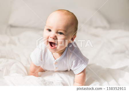 Smiling happy newborn baby on a white bed at home, the concept of a happy healthy infant baby. Generation alpha and gen alpha Smiling happy newborn baby on a white bed at home, the concept of a happy healthy infant baby. Generation alpha and gen alpha 138352911