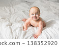 Smiling newborn baby on a white bed at home, the concept of a happy healthy infant baby. Generation alpha and gen alpha. Copy space 138352920