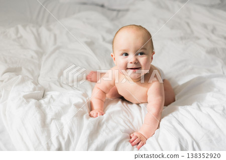Smiling newborn baby on a white bed at home, the concept of a happy healthy infant baby. Generation alpha and gen alpha. Copy space Smiling newborn baby on a white bed at home, the concept of a happy healthy infant baby. Generation alpha and gen alpha. Copy space 138352920