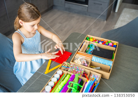 Top view of little girl making craft from wooden sticks at table using colorful materials. Kids creativity fine motor skills development and hands on learning concept. Top view of little girl making craft from wooden sticks at table using colorful materials. Kids creativity fine motor skills development and hands on learning concept. 138353050