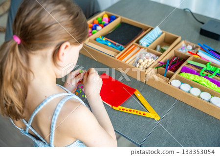 Little girl decorating handmade craft with colorful self adhesive rhinestones at table. Kids creativity fine motor skills development and learning through play concept. Little girl decorating handmade craft with colorful self adhesive rhinestones at table. Kids creativity fine motor skills development and learning through play concept. 138353054