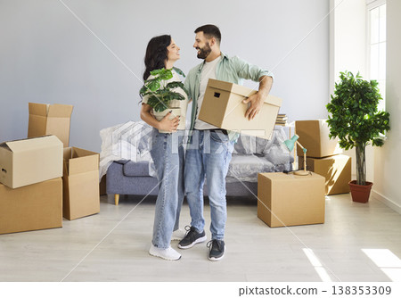 Happy family couple standing with moving box and houseplant in new apartment Happy family couple standing with moving box and houseplant in new apartment 138353309