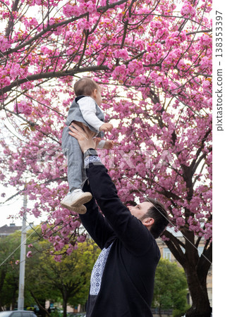 Father lifting baby under pink cherry blossoms in spring Father lifting baby under pink cherry blossoms in spring 138353397
