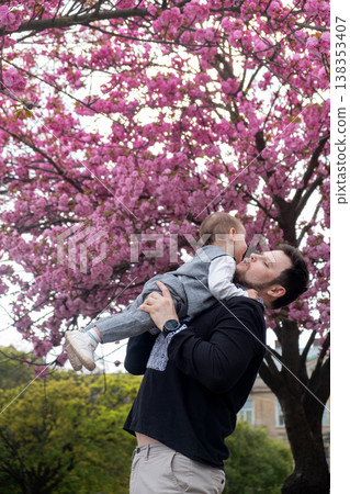 Father lifting baby under pink cherry blossoms in spring Father lifting baby under pink cherry blossoms in spring 138353407