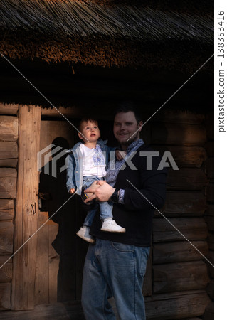Father holding toddler by rustic wooden cabin in sunlight Father holding toddler by rustic wooden cabin in sunlight 138353416