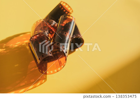 Unrolled 35mm photographic film negatives lay on bright yellow surface with shadows Unrolled 35mm photographic film negatives lay on bright yellow surface with shadows 138353475