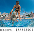 Mother helping toddler enter swimming pool on sunny vacation 138353504