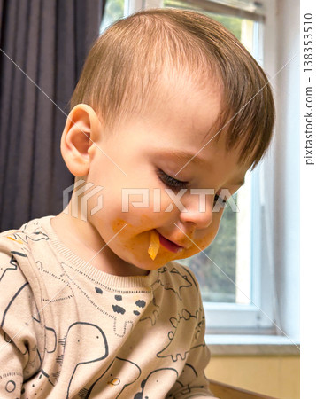 Toddler eating finger food with messy face indoors 138353510