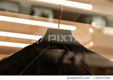 A black jacket is hung on a display hook in a retail store. Bright lights illuminate the jacket and create reflections on the glass. The setting is busy with light and activity A black jacket is hung on a display hook in a retail store. Bright lights illuminate the jacket and create reflections on the glass. The setting is busy with light and activity 138353580