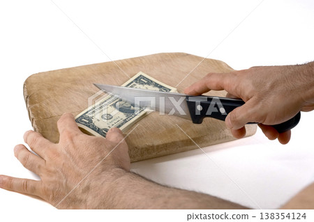 Cutting US dollar banknotes on a wooden chopping board with a knife Cutting US dollar banknotes on a wooden chopping board with a knife 138354124