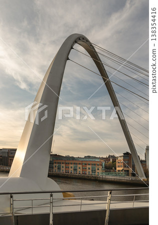 The sweeping arc of the Gateshead Millennium Bridge dominates this vertical frame, its pristine white steel slicing through a sky of soft, streaked clouds. Often called the "Blinking Eye," this The sweeping arc of the Gateshead Millennium Bridge dominates this vertical frame, its pristine white steel slicing through a sky of soft, streaked clouds. Often called the "Blinking Eye," this 138354416