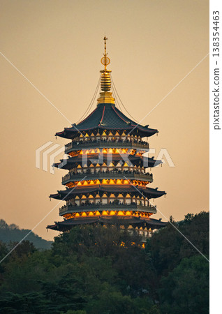 Traditional East Asian pagoda shining with warm lights at sunset, nestled among lush green trees on a tranquil hillside Traditional East Asian pagoda shining with warm lights at sunset, nestled among lush green trees on a tranquil hillside 138354463