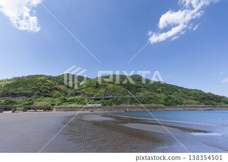 A JR Kyushu Nichinan Line Kiha 40 train runs across Sanno Beach in Nichinan City, Miyazaki Prefecture, under a clear blue sky. A JR Kyushu Nichinan Line Kiha 40 train runs across Sanno Beach in Nichinan City, Miyazaki Prefecture, under a clear blue sky. 138354501