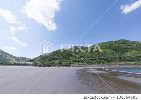 A JR Kyushu Nichinan Line Kiha 40 train runs across Sanno Beach in Nichinan City, Miyazaki Prefecture, under a clear blue sky. A JR Kyushu Nichinan Line Kiha 40 train runs across Sanno Beach in Nichinan City, Miyazaki Prefecture, under a clear blue sky. 138354506