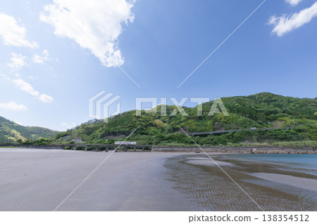 A JR Kyushu Nichinan Line Kiha 40 train runs across Sanno Beach in Nichinan City, Miyazaki Prefecture, under a clear blue sky. 138354512
