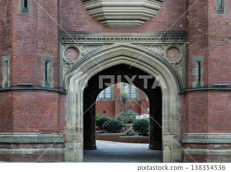 The archway of the King Edward VII Building acts as a weathered threshold, carved from stone and wrapped in deep crimson brick. Its pointed Gothic curve offers a glimpse into a tranquil courtyard The archway of the King Edward VII Building acts as a weathered threshold, carved from stone and wrapped in deep crimson brick. Its pointed Gothic curve offers a glimpse into a tranquil courtyard 138354536