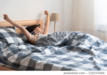 An adult woman feeling refreshed and well-rested, stretching after waking up in morning her arms above her head after waking up comfortably in bed. Authentic lifestyle An adult woman feeling refreshed and well-rested, stretching after waking up in morning her arms above her head after waking up comfortably in bed. Authentic lifestyle 138355000