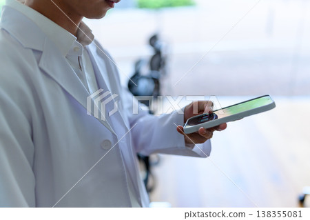 A person in a white coat is operating a smartphone. A person in a white coat is operating a smartphone. 138355081