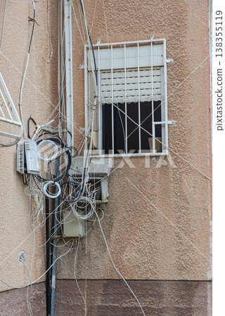 Disordered cables and wires installed on exterior wall of residential building. Urban infrastructure and chaotic wiring concept. Disordered cables and wires installed on exterior wall of residential building. Urban infrastructure and chaotic wiring concept. 138355119
