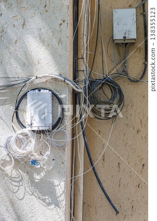 Disordered cables and wires installed on exterior wall of residential building. Urban infrastructure and chaotic wiring concept. Disordered cables and wires installed on exterior wall of residential building. Urban infrastructure and chaotic wiring concept. 138355123