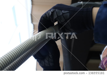 A worker with black rubber gloves is performing indoor plumbing work, holding corrugated tubing. 138355181