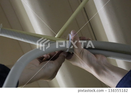 A worker's hands running corrugated tubing wiring to a wooden beam in the ceiling. A worker's hands running corrugated tubing wiring to a wooden beam in the ceiling. 138355182