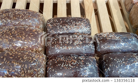 Assorted dark rye and whole grain bread loaves topped with seeds in retail packaging on wooden rack 138356118