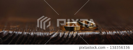 Banner Two gold wedding rings on dark wooden surface with dark background Banner Two gold wedding rings on dark wooden surface with dark background 138356336