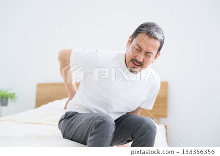 Japanese man suffering from lower back pain while in bed Japanese man suffering from lower back pain while in bed 138356356