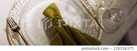 Banner Green cloth napkin with gold ring on white glass plate on dark background Banner Green cloth napkin with gold ring on white glass plate on dark background 138356375