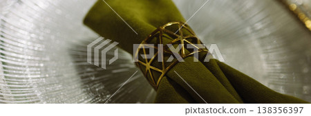 Banner Green cloth napkin with gold ring on white glass plate on dark background Banner Green cloth napkin with gold ring on white glass plate on dark background 138356397