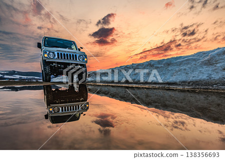 A stunning scene of a winter sunset reflected in a puddle, with a car beautifully illuminated. 138356693