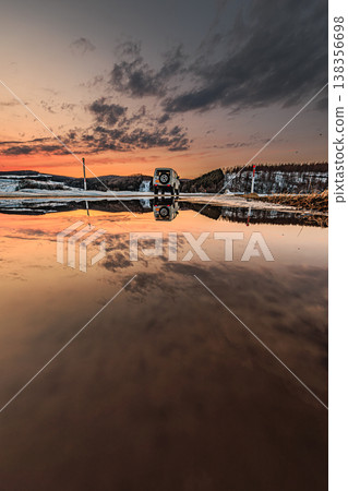 Snow walls, sunset sky, and an off-road vehicle reflected on the calm surface of the water. 138356698