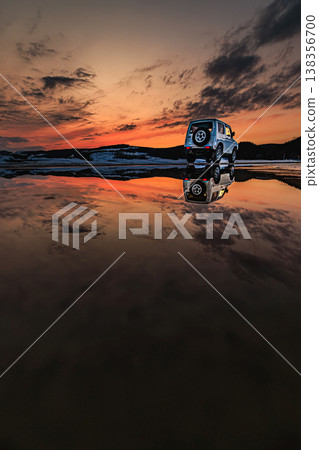 A snowy road bathed in the sunset, with the reflection of a car in a puddle. 138356700