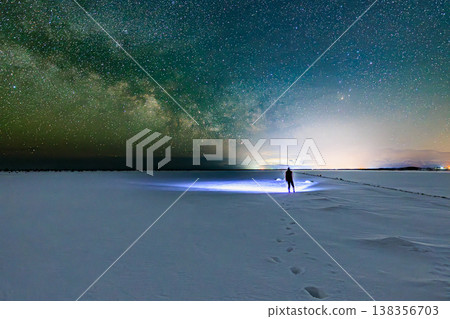 The Milky Way shines in the winter night, the snowy plains and the distant city lights. 138356703