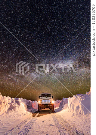 A road surrounded by snow walls, the Milky Way, and a four-wheel drive vehicle under a starry sky. 138356709