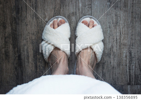 White soft slippers on women feet, top view. Homey clothing. Cozy fluffy slippers on legs, view from above. Domestic lifestyle. Cozy clothes in spa salon. Woman after bathroom. Pair of fluffy shoes 138356895