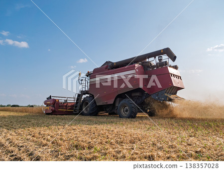 A combine harvester working in a vast agricultural field during a sunny daytime harvest, kicking up dust A combine harvester working in a vast agricultural field during a sunny daytime harvest, kicking up dust 138357028