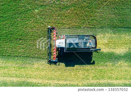 Aerial view captures powerful combine harvester gathers crops on a vast green field under a clear blue sky during a sunny day near Aerial view captures powerful combine harvester gathers crops on a vast green field under a clear blue sky during a sunny day near 138357032