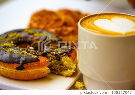 Dubai-style donuts with chocolate glaze topped with chopped pistachios, coffee 138357042