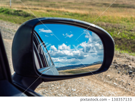 View of landscape reflected in side mirror while driving on gravel road View of landscape reflected in side mirror while driving on gravel road 138357133