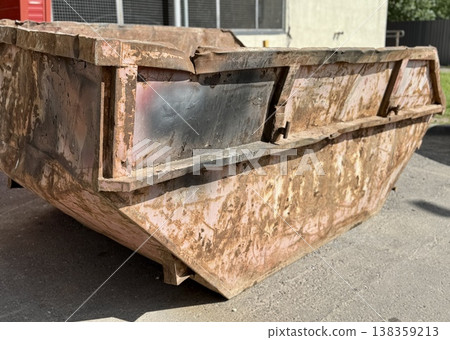 An old rusty dumpster sitting on a bustling city street filled with urban life and debris. The dumpster resting on the pavement clearly shows numerous signs of urban decay and waste management issues. An old rusty dumpster sitting on a bustling city street filled with urban life and debris. The dumpster resting on the pavement clearly shows numerous signs of urban decay and waste management issues. 138359213