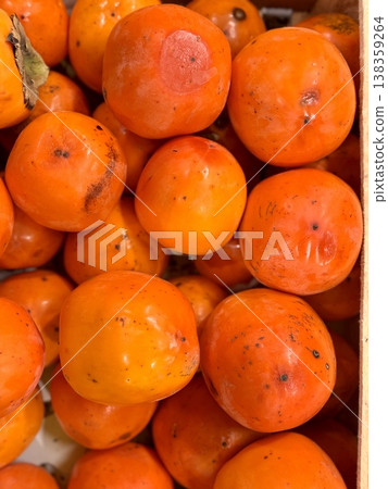 A pile of ripe juicy orange persimmons in a box, offered for sale at a supermarket vegetable stand, demonstrates organic, vegetarian and healthy food. Close-up. A pile of ripe juicy orange persimmons in a box, offered for sale at a supermarket vegetable stand, demonstrates organic, vegetarian and healthy food. Close-up. 138359264
