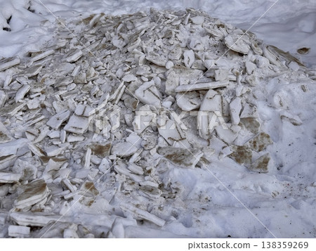 A pile of shattered ice pieces is scattered on a snowcovered ground, showcasing winters unique and beautiful textures. 138359269