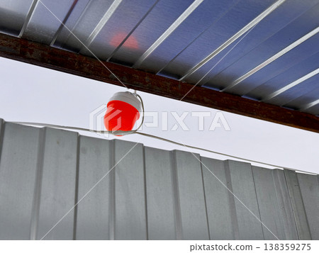 A vivid red lantern is gracefully suspended beneath a roof, casting a warm, inviting light over a cozy sheltered area 138359275