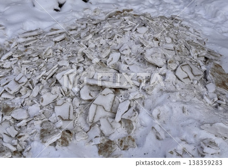 A pile of shattered ice pieces is scattered on a snowcovered ground, showcasing winters unique and beautiful textures. 138359283