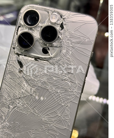 ALMATY, KAZAKHSTAN - FEBRUARY 27, 2025: The back of a broken glass silver side of a broken iPhone 14 Pro displayed on a showcase shelf in an electronics store. Close-up. 138359305