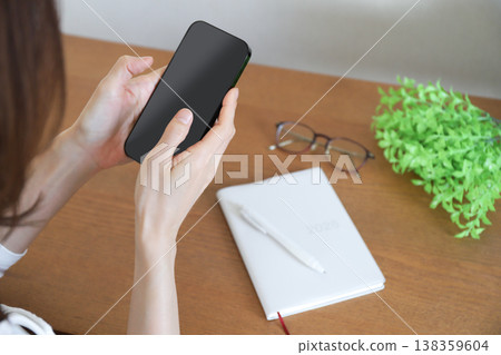 A woman operating a smartphone and a notebook A woman operating a smartphone and a notebook 138359604