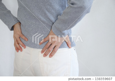 一名女子因背痛而摀著下背部。 一名女子因背痛而摀著下背部。 138359607