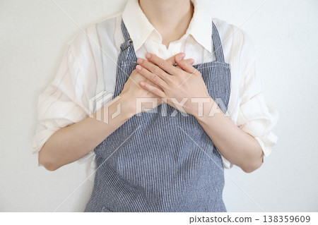 A woman in an apron with her hand on her chest A woman in an apron with her hand on her chest 138359609